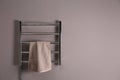 Modern heated towel rail with warm soft towel on grey wall. Space for text