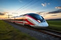 A modern high-speed train moves along the railway tracks against the backdrop of a field at sunset. High-speed rail transport