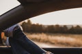 Modern hipster girl resting in a car and admiring view. Woman driver watching sunset put feet on car door. Feet outside the window Royalty Free Stock Photo