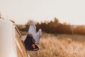 Modern hipster girl resting in a car and admiring view. Woman driver watching sunset put feet on car door. Feet outside the window Royalty Free Stock Photo