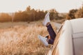 Modern hipster girl resting in a car and admiring view. Woman driver watching sunset put feet on car door. Feet outside the window Royalty Free Stock Photo