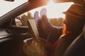 Modern hipster girl resting in a car and reading a map. Woman with feet on car door. Feet outside the window at sunset Royalty Free Stock Photo