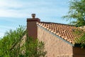 Modern home with cement exterior and adobe orange roof tiles with visible chimney with metal vents and back yard trees Royalty Free Stock Photo