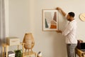 Modern home decor and interior design. Young black man hanging painting, putting picture frame on wall indoors Royalty Free Stock Photo