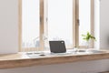 Modern home office with wooden tabletop, modern laptop, city view from the window, white coffee mug and lamp and glass vase