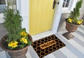 Modern honeycomb patterned yellow black welcome zute doormat outside home with yellow flowers and leaves Royalty Free Stock Photo
