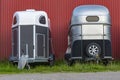 Modern horse transportation trailers parked on the grass near red scandinavian swedish hangar shed house