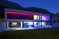 Modern house with swimming pool and garden in night scene illuminated by colored LED lights. Behind the house is the hill with the Royalty Free Stock Photo