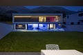 Modern house with swimming pool and garden in night scene illuminated by colored LED lights. Behind the house is the hill with the Royalty Free Stock Photo