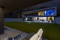 Modern house with swimming pool and garden in night scene illuminated by colored LED lights. In the foreground is a patio with a Royalty Free Stock Photo