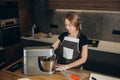 Beautiful confectioner girl dressed in apron standing in the kitchen whipping cream with a mixer