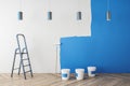 Modern interior with blue paint on concrete wall, painting tools, ladder, lamps and wooden flooring. Repairs concept.