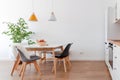 Modern interior of cozy kitchen, dining room, white furniture, lamps above wooden table, chairs, apples, bowl. Concept