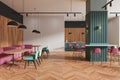 Modern interior design of a cafe with pink and teal chairs, wooden elements, herringbone flooring, and pendant lighting on a