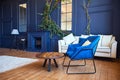 Modern interior with a fireplace, a spacious living room with blue walls and wooden floors, a blue armchair in the foreground and