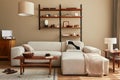 Modern interior of living room with design modular beige sofa, coffee table, furniture, pendant lamp, shelf, slippers, carpet.