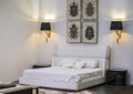Modern interior, white bedroom with a double bed, paintings and lamps on the walls. Beautiful design of the bedroom
