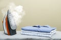 Modern iron with steam and folded clothes on ironing board, space for text Royalty Free Stock Photo