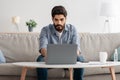 Modern job. Concentrated arab man working on laptop at home office, sitting on sofa and using computer Royalty Free Stock Photo