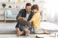 Modern kids interests. Cute little boy watching his daddy working on laptop, cheerful man showing son how to work online Royalty Free Stock Photo