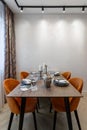 Modern kitchen combined with the dining room in dark and light colors, with orange chairs and glass cabinets for dishes