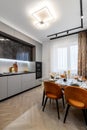 Modern kitchen combined with the dining room in dark and light colors, with orange chairs and glass cabinets for dishes