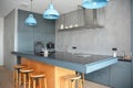 A modern kitchen design with gray walls, glass and gray kitchen cabinets, wooden stools, a black kitchen island, and blue lamps Royalty Free Stock Photo