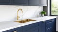 A modern kitchen with navy blue cabinets and a golden faucet highlights fresh plants by the window, creating a bright