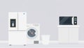 A modern kitchen scene featuring a white refrigerator, washing machine, microwave, and a trash bin on a light gray Royalty Free Stock Photo