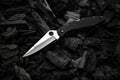 Modern knife with a silver blade. Hunting, military folding knife on smoldering charcoal. Black back