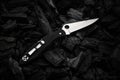 Modern knife with a silver blade. Hunting, military folding knife on smoldering charcoal. Black back