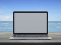 Modern laptop computer with blank grey screen on wooden table over tropical sea and blue sky with white clouds Royalty Free Stock Photo