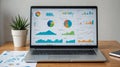 Modern laptop displaying colorful infographics including pie charts, bar graphs, and line charts on screen, placed on a wooden Royalty Free Stock Photo