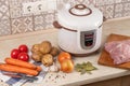 Modern, light multi cooker and products on table in kitchen. Cooking stewed potatoes with meat in multicooker Royalty Free Stock Photo