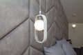 Modern lit, white lamp, illuminator with geometry oval decorative element, soft fabric head of bed, bedroom interior design