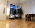 Modern living room with real oak hardwood floors, piano, fireplace and large windows during late evening Royalty Free Stock Photo