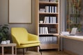 A modern living room with a yellow armchair, a wooden bookshelf, and a table against the window Royalty Free Stock Photo