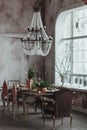 Modern loft dining room with high ceiling, vintage armchairs, empty grey concrete wall, wooden floor, dining table with