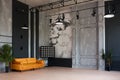 Modern loft living room with high ceiling, black and grey walls, wooden floor, design furniture and tropical plant.