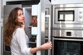Modern beautiful long haired woman standing in the kitchen and open refrigerators door and looking at camera.