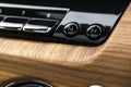 Modern luxury car white interior with natural wood panel. Part of car dashboard. Interior of prestige modern car. Media control bu