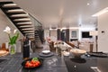 Modern luxury open-plan interior featuring a floating staircase, marble dining table, wooden kitchen, and beige sofa Royalty Free Stock Photo