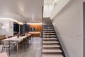 Modern luxury open-plan interior featuring a floating staircase, marble dining table, wooden kitchen, and beige sofa Royalty Free Stock Photo