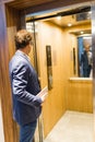 Businessman with digital tablet entering modern wooden elevator