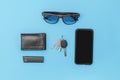 Modern man items don`t forget to carry in top view on table cell phone sunglasses lighter wallet keys in black on blue background