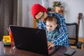 Modern man is working on a laptop, and his little son is sitting on his lap. Concept of family and remote work from home