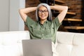 Modern mature 60s female enjoy leisure weekend at home, watching movie on computer gadget. Happy elderly woman sit relax Royalty Free Stock Photo