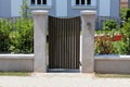 Modern metal entrance doors mounted on concrete poles surrounded with narrow metal fence and stone tiles in front