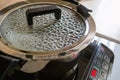 Modern metal soup pot or pan with black handles on an induction stove. Drops of boiling water are on inner surface of transparent