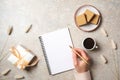 Modern minimal home workspace desk with human hand writing text message on blank paper notebook, waffles, dry flowers on concrete Royalty Free Stock Photo